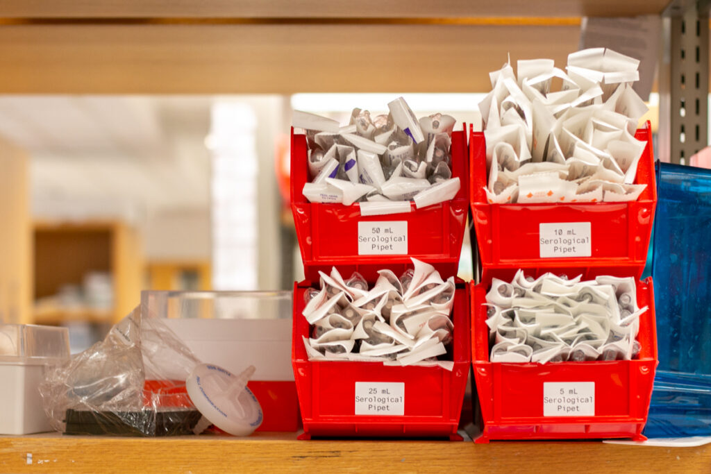 Different sizes of serological pipets in buckets on a shelf.