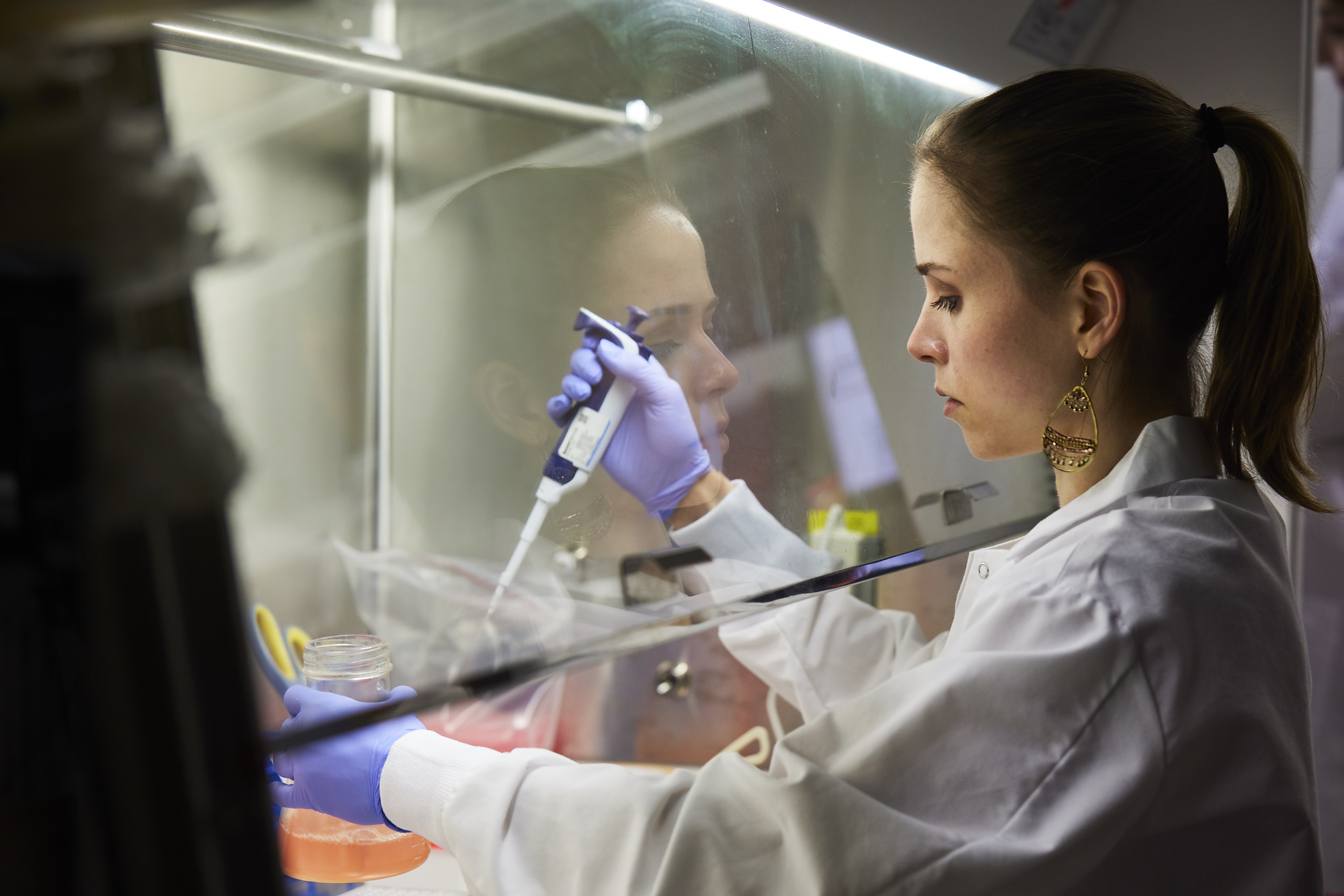 Woman in lab coat feeding cell lines under hood.