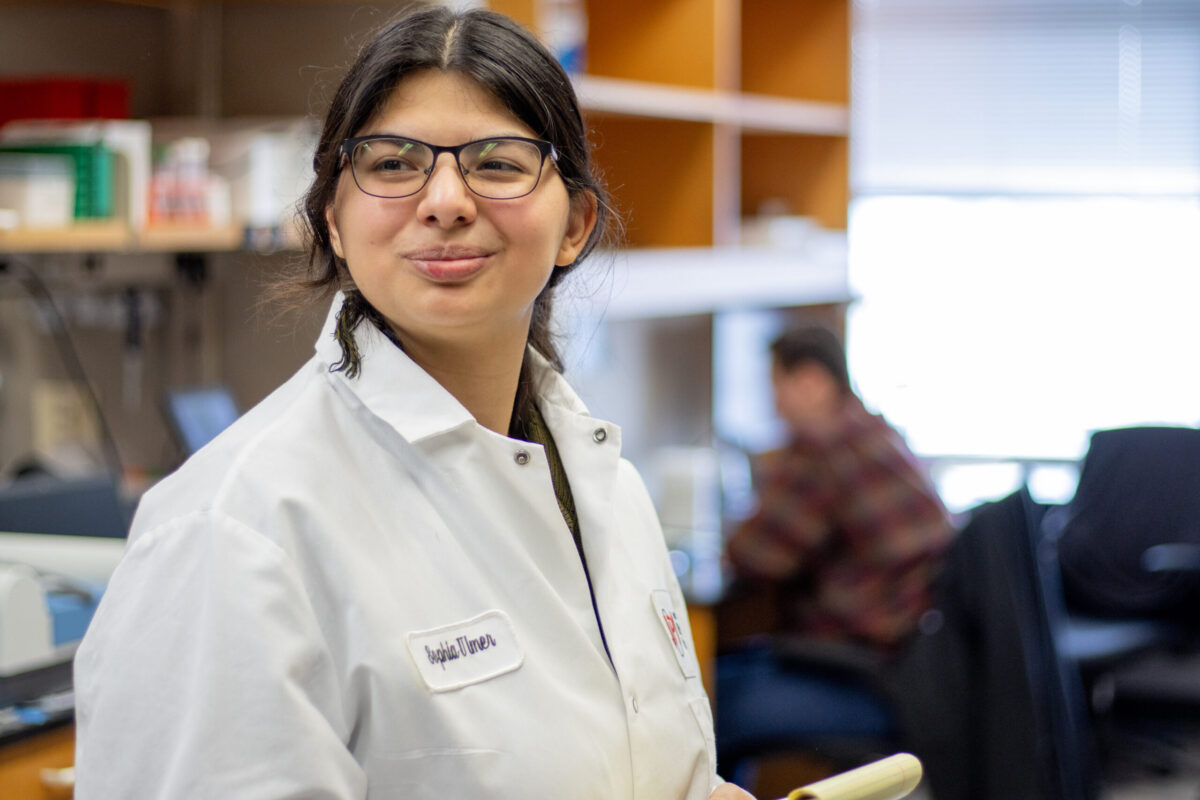 Woman in glasses wearing lab coat holding pad of paper.