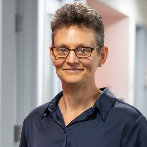 Deborah Moshinsky, pictured smiling in an office wearing a collared shirt, glasses and earrings.