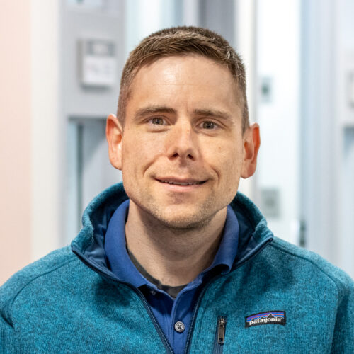 Man smiles for headshot in office setting.