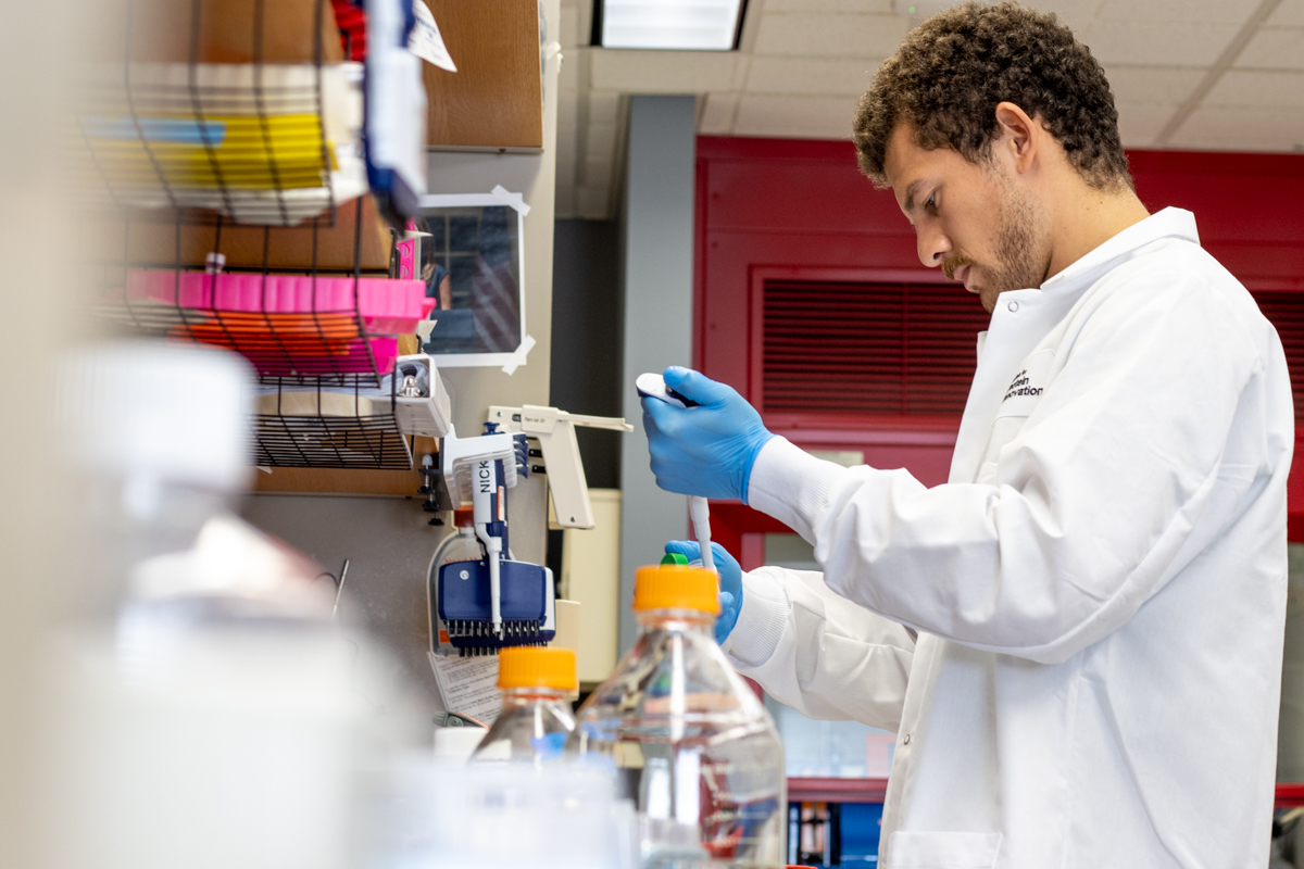 A man in a lab coat working at a lab bench filled with bottles.