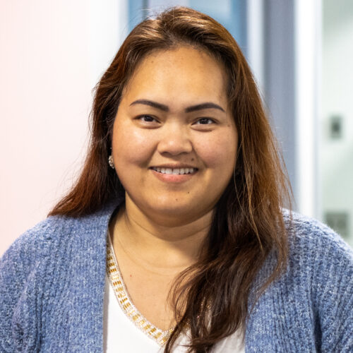 Sophea Sann-Rorth, wearing a white shirt and blue sweater, smiles in the IPI office.