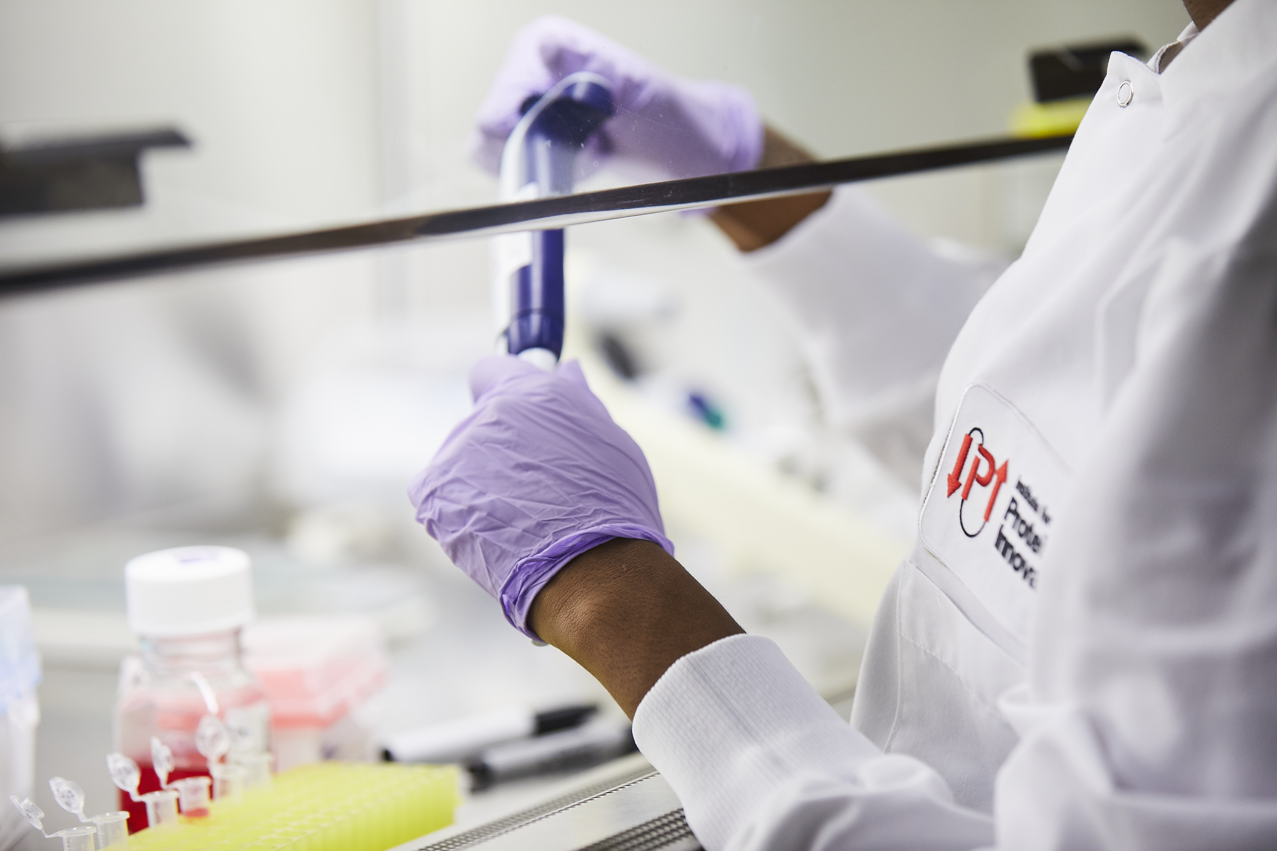 Scientist wearing IPI lab coat holds pipette under fume hood.