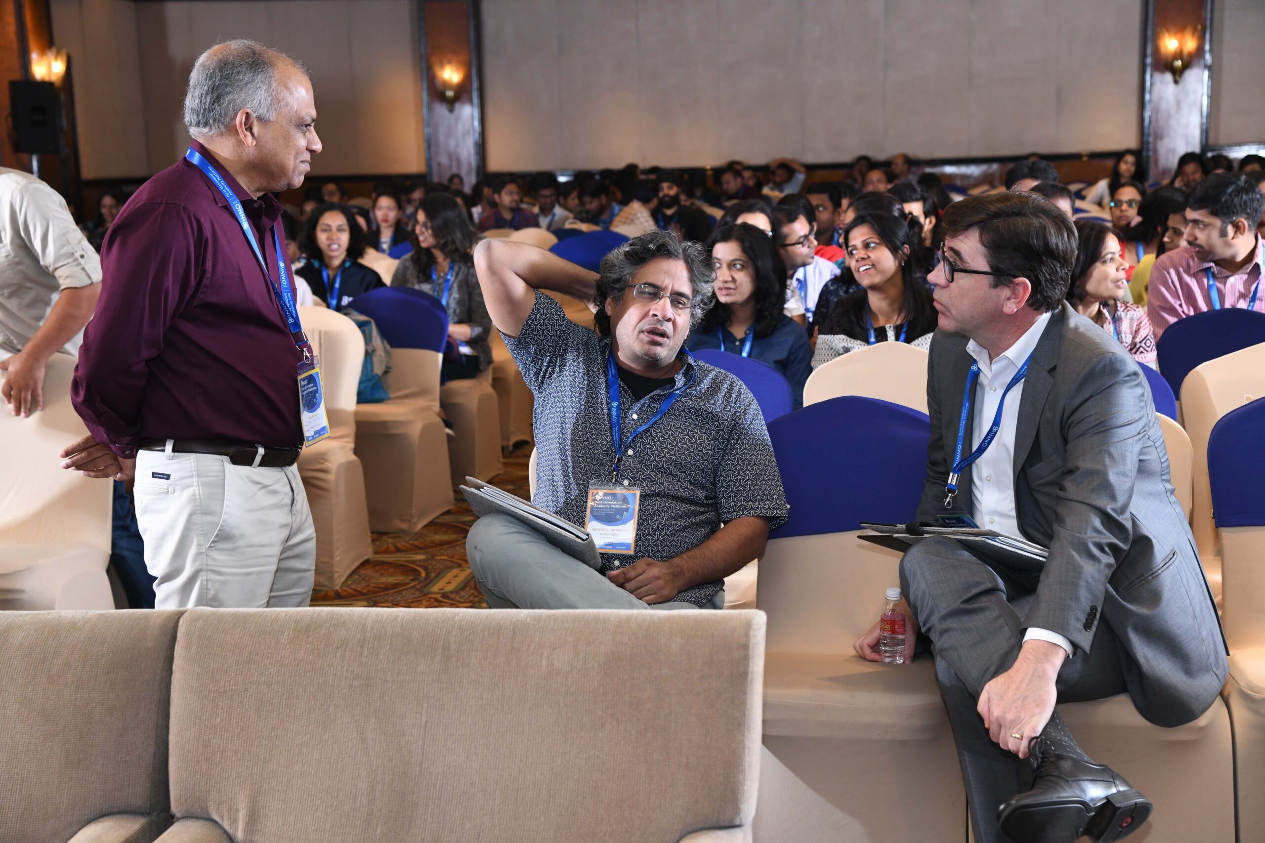 Three people sit in chairs in a conference room, talking.