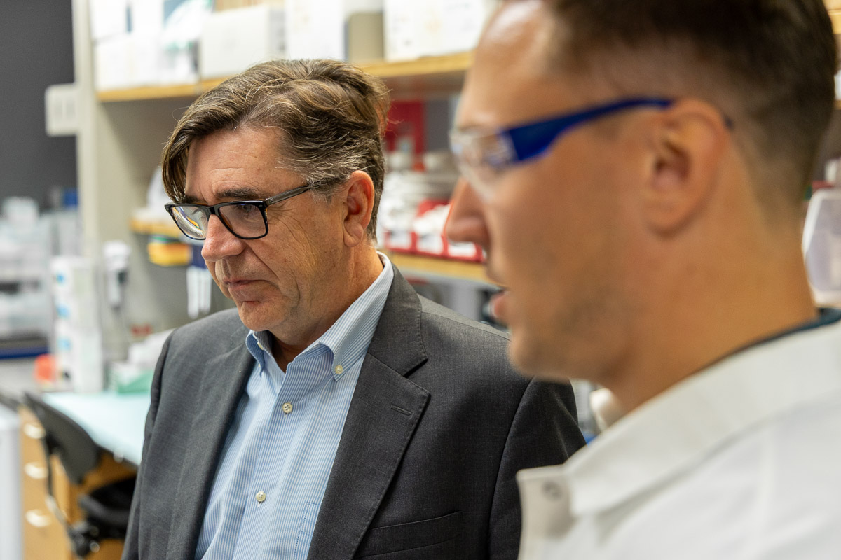 Kevin Harvey speaks with a scientist in lab coat and goggles.